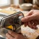 Person inspecting a stainless steel manual pasta machine on a kitchen counter.