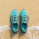A pair of budget-friendly water shoes resting on sandy beach near ocean waves.