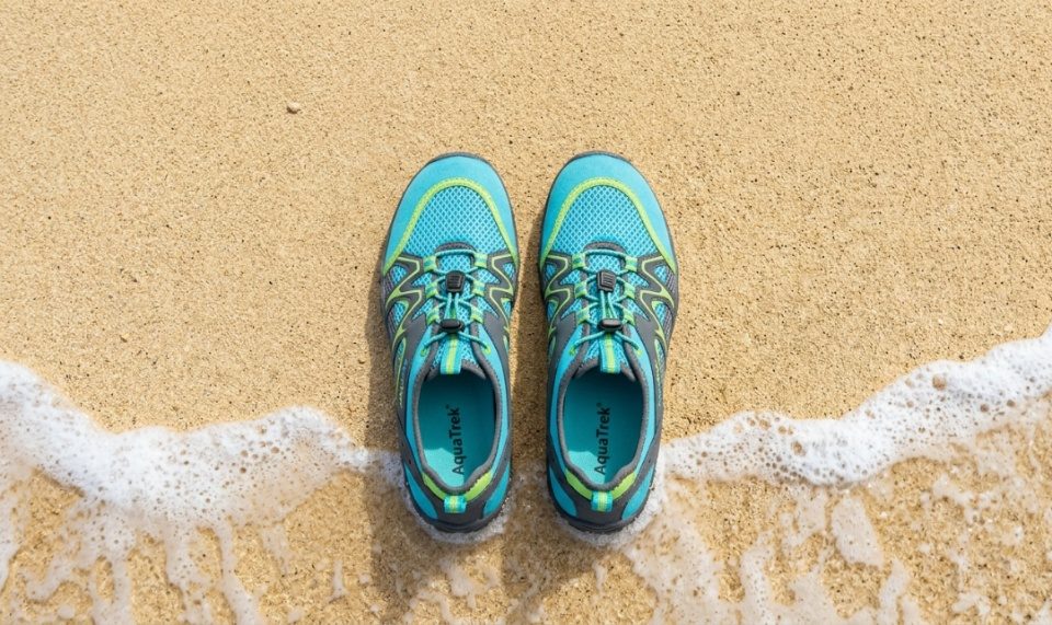 A pair of budget-friendly water shoes resting on sandy beach near ocean waves.